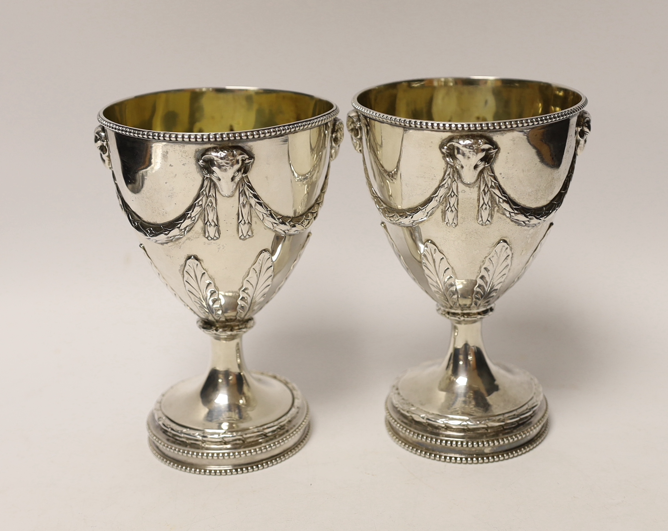 A pair of late George III silver goblets, with ram's head and swag decoration, maker H.G, London, 1816, 15.1cm, 16.3oz, with partly erased engraved inscriptions.